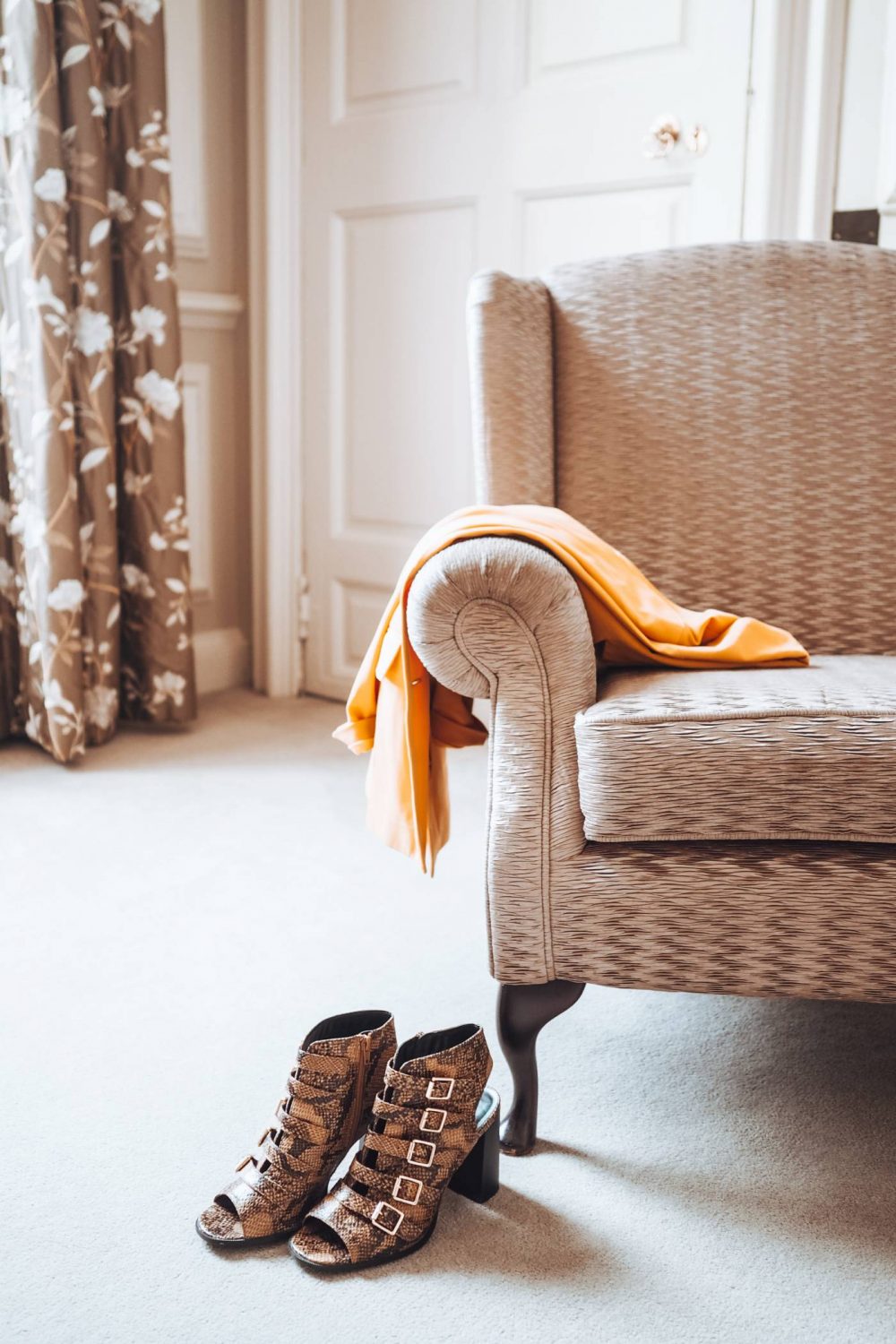 Snake print peep toe ankle boots in front of an armchair with a yellow blazer over it