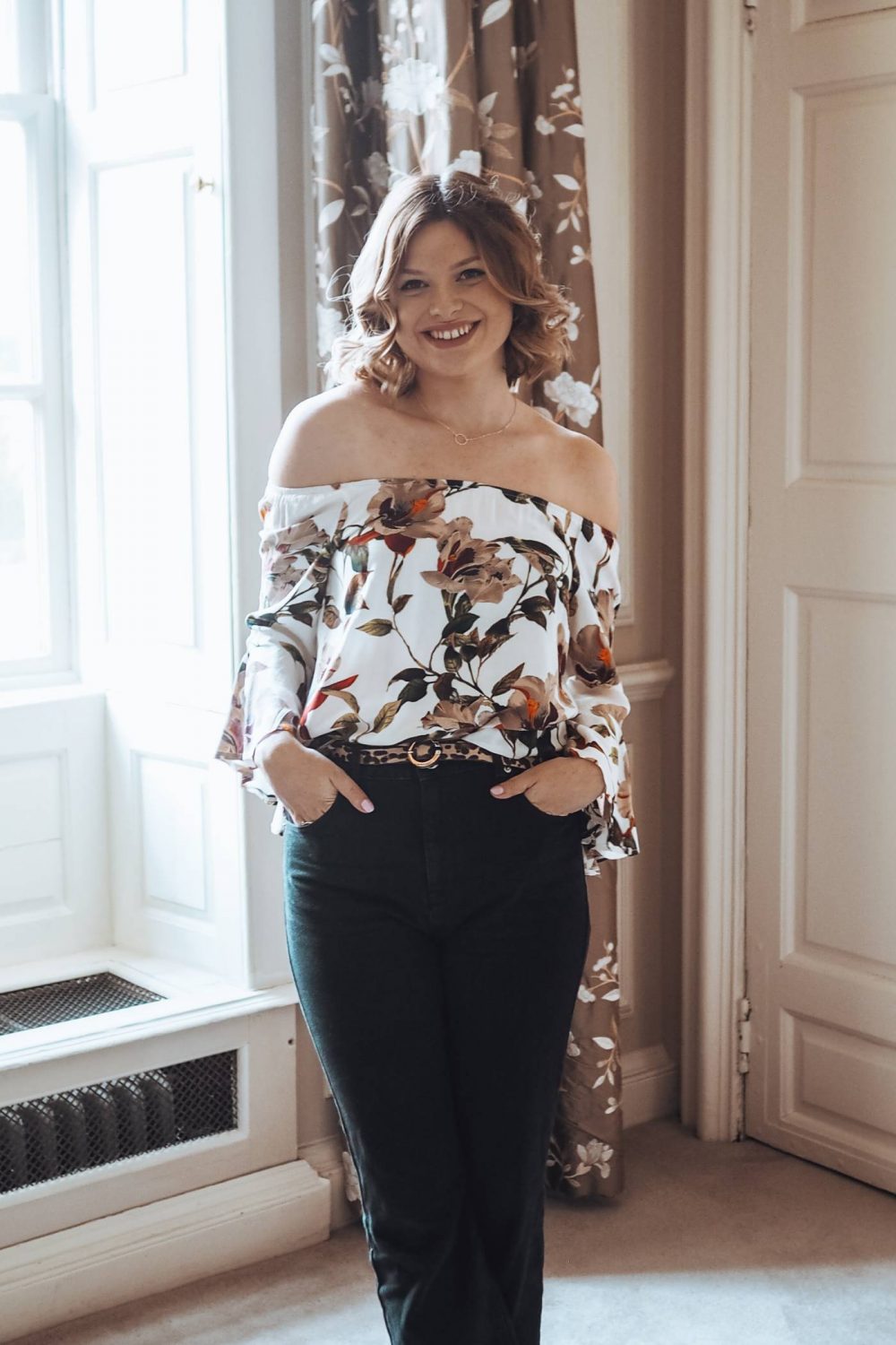 Sophie wearing a floral off the shoulder blouse in her room at Chicheley Hall