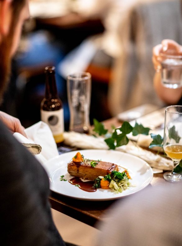A photo of pork belly over someone's shoulder at The Brasserie