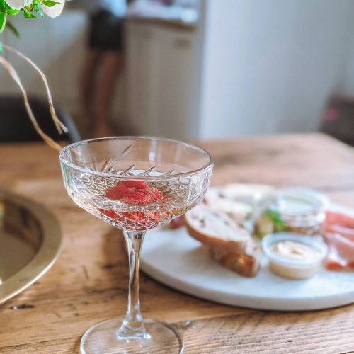 A photo of a crystal cut champagne saucer filled with champagne and raspberries