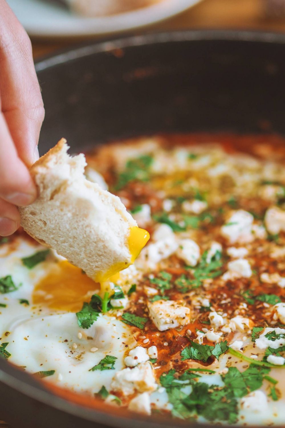 Someone dipping bread into a runny egg yolk in shakshuka