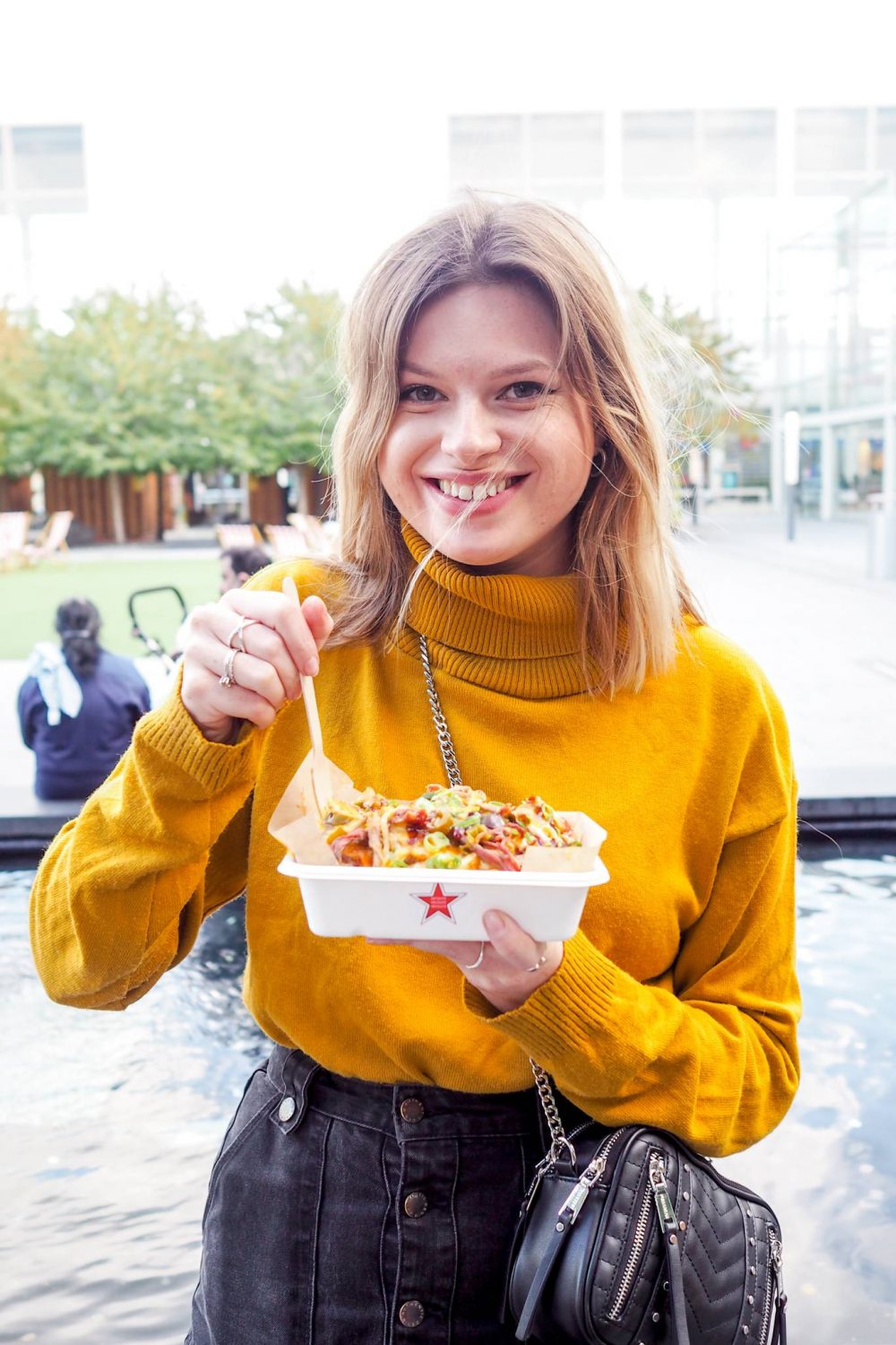 Sophie is in a yellow jumper eating loaded fries from Fry Guys MK who are based in Queen's Court Market